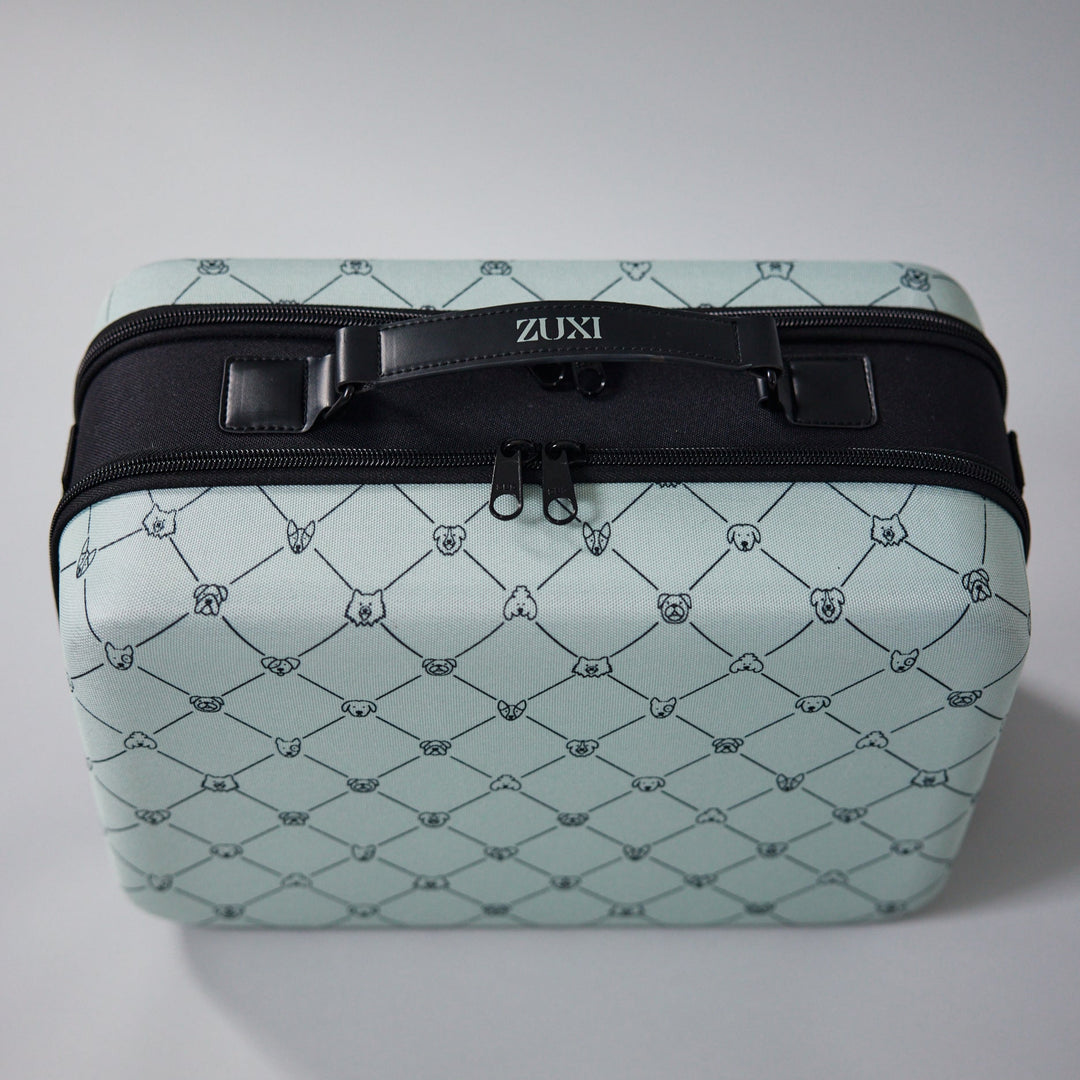 ZUXI travel case in sage green dog-face diamond print fabric with a black top handle bearing the ZUXI logo and a black zippered opening, viewed from the front.
