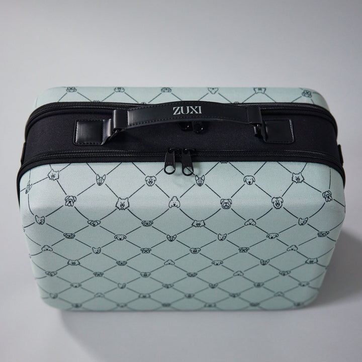 ZUXI travel case in sage green dog-face diamond print fabric with a black top handle bearing the ZUXI logo and a black zippered opening, viewed from the front.