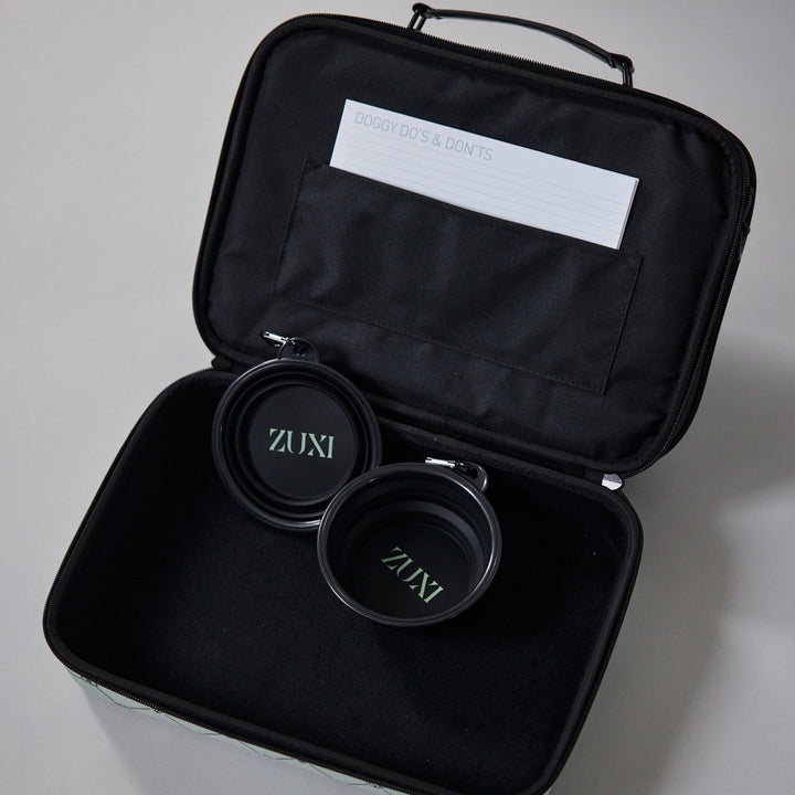 Open black ZUXI travel case showing two nested collapsible black travel bowls with the ZUXI logo, and a "Doggy Do's & Don'ts" card tucked into the interior pocket.