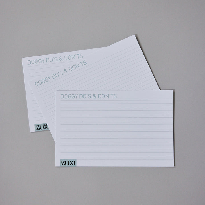 Stack of ZUXI "Doggy Do's & Don'ts" printed care instruction cards with the ZUXI logo, laid on a gray background.