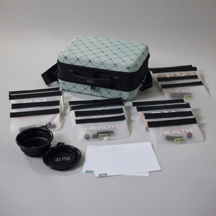 A pet travel kit laid out on a light gray surface, including a sage green and black patterned carrying case, several clear zippered pouches with black bands labeled 'HEALTH' , "TREATS", "AM" ans 'PM', two collapsible bowls, three white note cards labeled DOGGY DO'S AND DONT'S