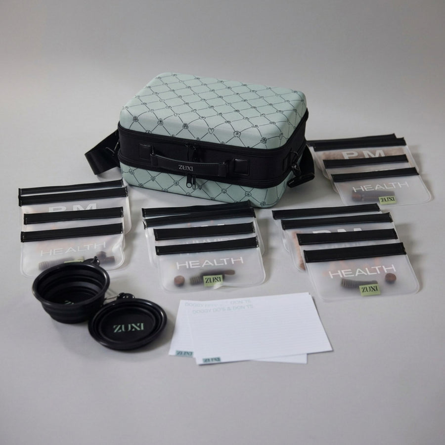 A pet travel kit laid out on a light gray surface, including a sage green and black patterned carrying case, several clear zippered pouches with black bands labeled 'HEALTH' , "TREATS", "AM" ans 'PM', two collapsible bowls, three white note cards labeled DOGGY DO'S AND DONT'S